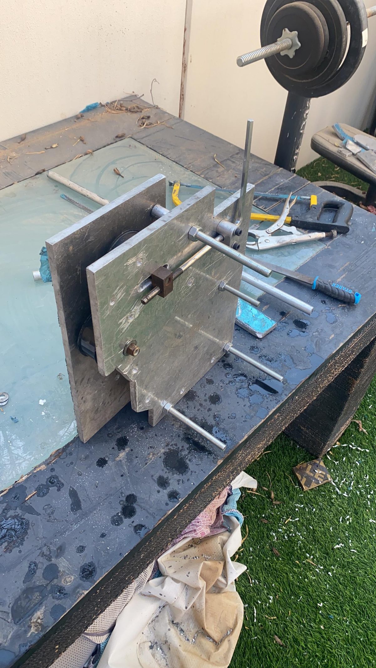 Aluminum bracket plates clamped on the bench with threaded rods, gym weight as a brace.