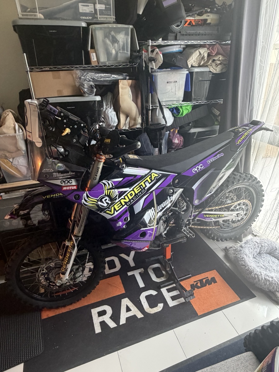 Vendetta Racing rally bike #3 in the Dubai garage. Purple Vendetta livery, Milwaukee sponsor, KTM Ready to Race mat under the wheels.