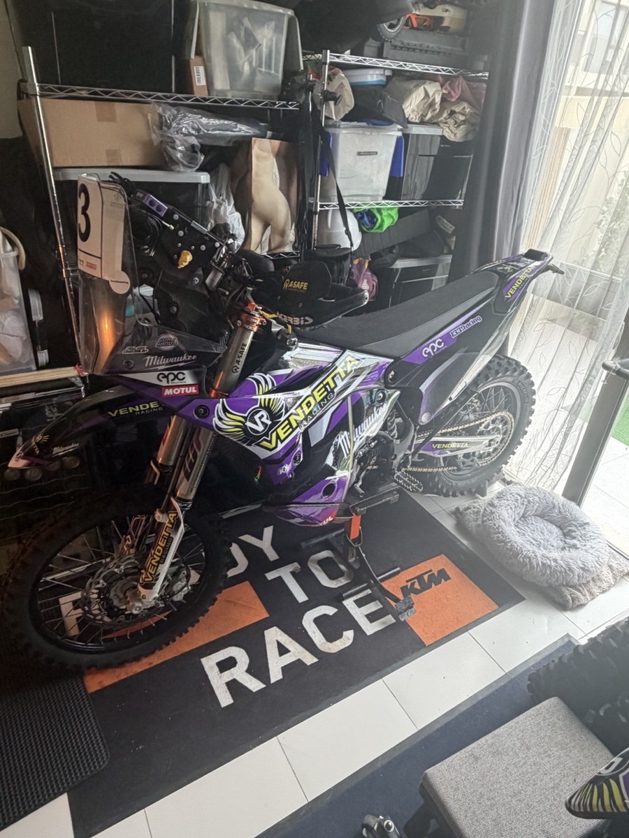 Vendetta Racing rally bike #3 in the Dubai garage. Purple Vendetta livery, Milwaukee sponsor, KTM Ready to Race mat under the wheels.