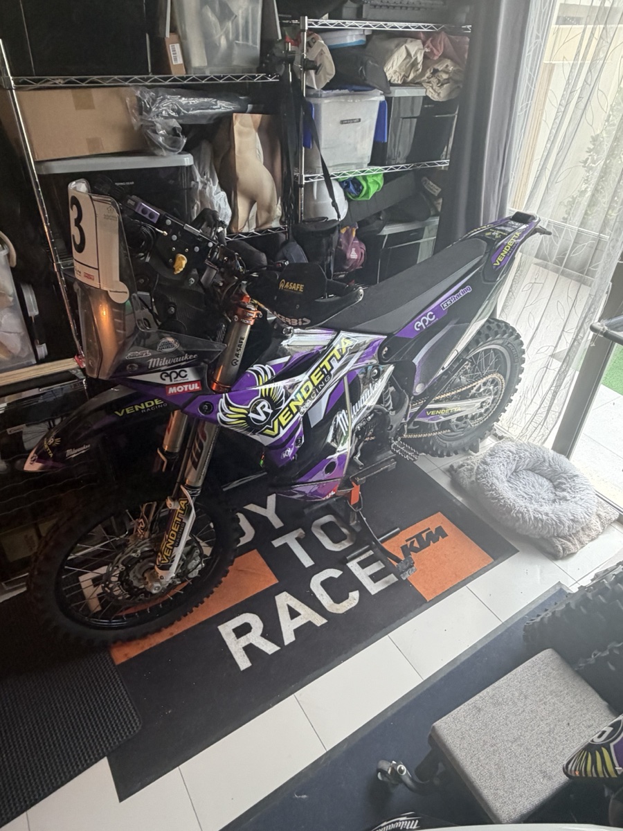Vendetta Racing rally bike #3 in the Dubai garage. Purple Vendetta livery, Milwaukee sponsor, KTM Ready to Race mat under the wheels.