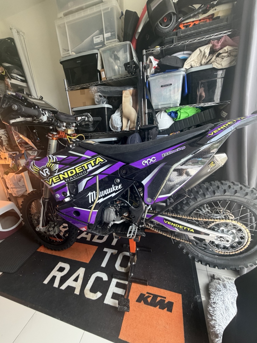 Vendetta Racing rally bike #3 in the Dubai garage. Purple Vendetta livery, Milwaukee sponsor, KTM Ready to Race mat under the wheels.
