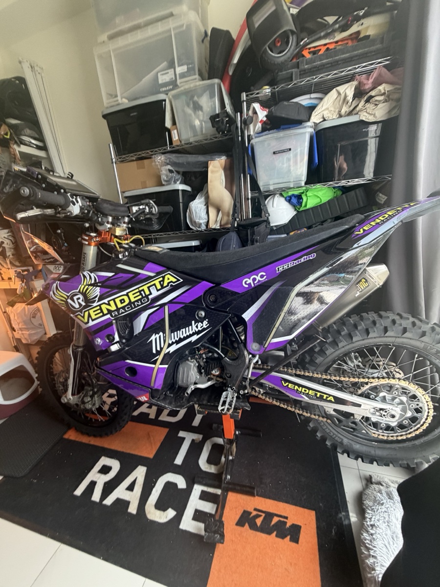 Vendetta Racing rally bike #3 in the Dubai garage. Purple Vendetta livery, Milwaukee sponsor, KTM Ready to Race mat under the wheels.