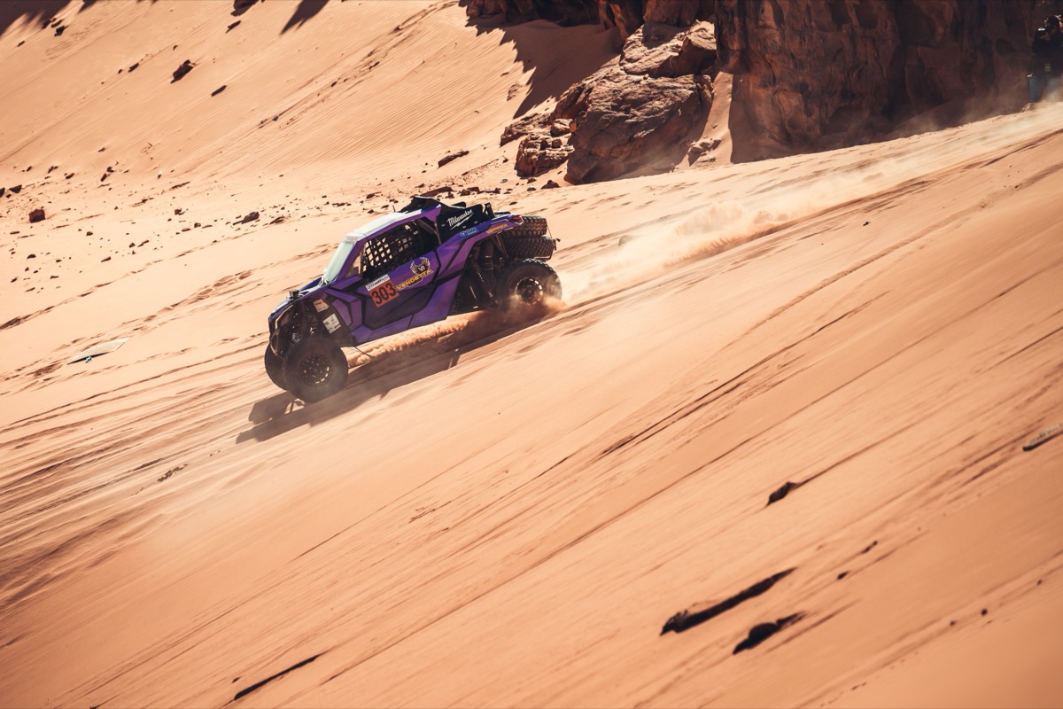 Vendetta Racing UTV #303 carving across a sand dune face, photographer just visible on the rocks.